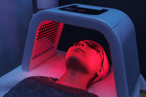 Person receiving red light therapy under a machine with a dark background